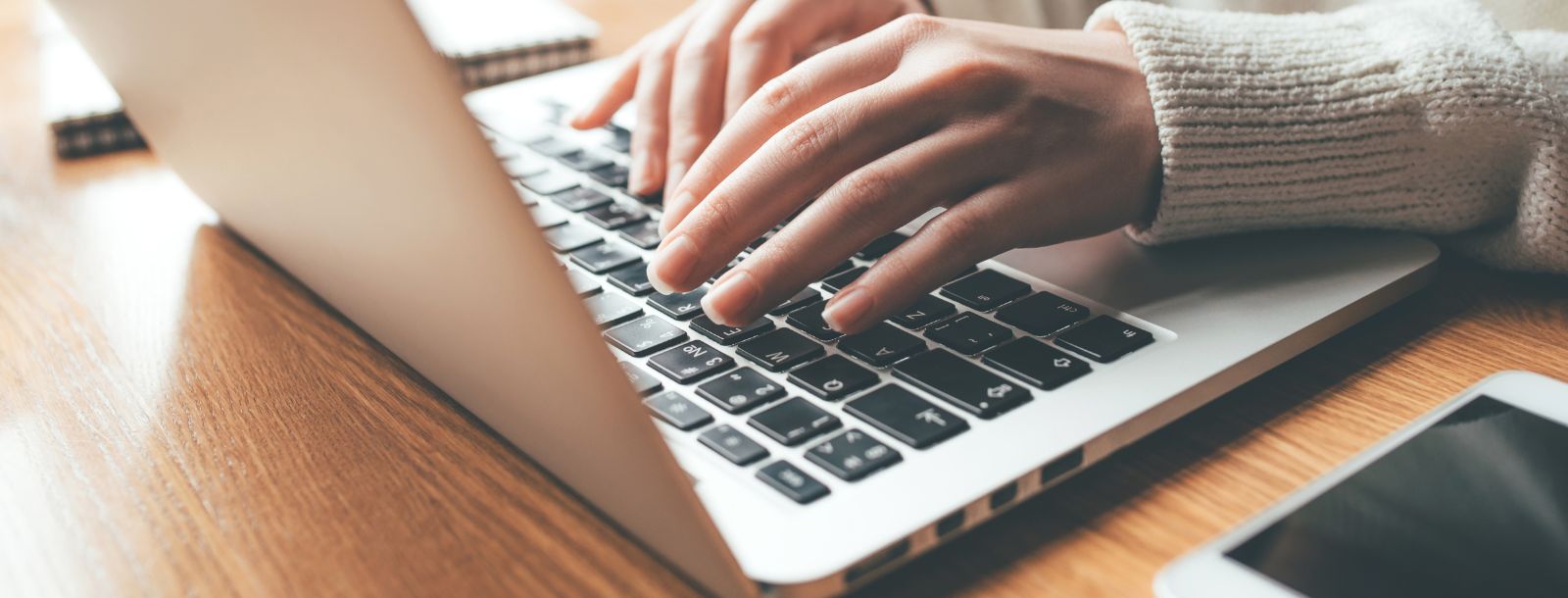 typing on laptop with cell phone next to it